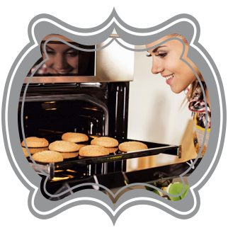 A woman smiling and removing a hot baking pan with cookies on it from her oven.